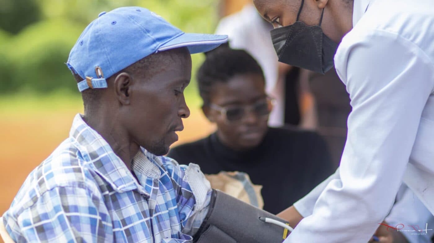 A man has his blood pressure taken at an outdoor community screening while health workers attend to others around him.